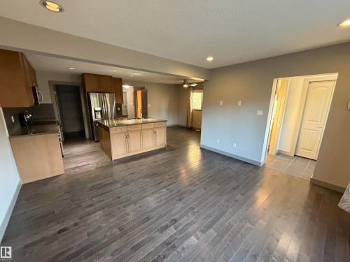 Open-concept living space featuring wood-finish flooring, recessed lighting, a kitchen island with storage, light wood cabinetry, and stainless steel appliances - 7065 Cardinal Way Sw, Edmonton, AB 
