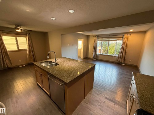 Spacious open concept interior with wood-finish flooring, recessed lighting, and a kitchen island featuring a double-basin sink and stainless steel dishwasher - 7065 Cardinal Way Sw, Edmonton, AB 