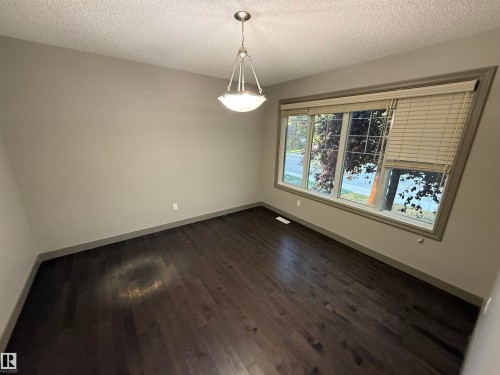 Dark wood-finish flooring with light-toned walls, featuring a wide window with blinds - 7065 Cardinal Way Sw, Edmonton, AB 