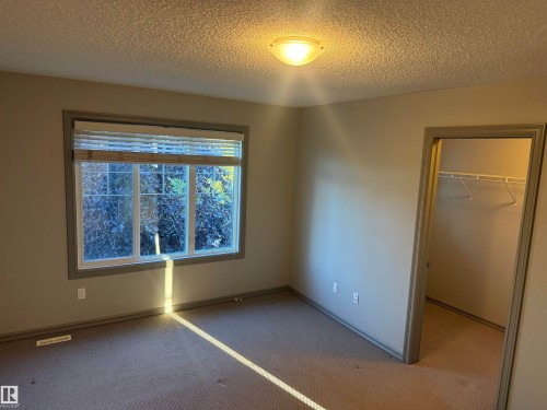 Carpeted room featuring a ceiling-mounted light fixture, a wide window with blinds, and a built-in closet with wire shelving - 7065 Cardinal Way Sw, Edmonton, AB 