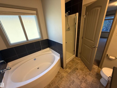 Soaking tub with chrome fixtures, tiled shower stall, and patterned floor tiling - 7065 Cardinal Way Sw, Edmonton, AB 