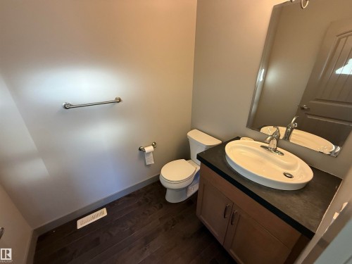 Wood-finish flooring, wall-mounted mirror, vanity with storage, vessel sink, and chrome fixtures - 7065 Cardinal Way Sw, Edmonton, AB 