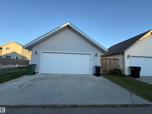 Attached garage with two overhead doors, light-toned siding, two exterior sconce lights, and a concrete driveway - 7065 Cardinal Way Sw, Edmonton, AB 