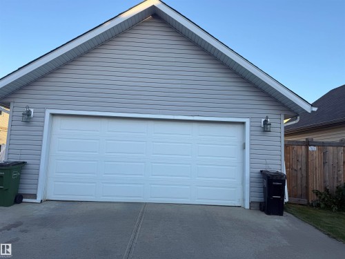Attached garage with a panel-style door, light gray siding, and exterior lighting fixtures - 7065 Cardinal Way Sw, Edmonton, AB 