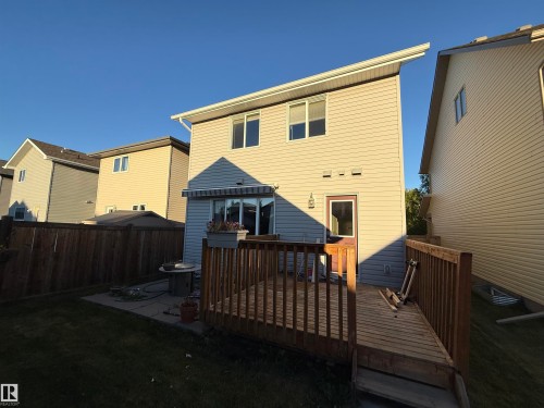 Exterior featuring light-colored siding, multiple windows, a rear entry door, and a wooden deck - 7065 Cardinal Way Sw, Edmonton, AB 
