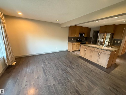 Expansive wood-finish flooring, recessed lighting, kitchen island with built-in storage, stainless steel appliances, and wood cabinetry - 7065 Cardinal Way Sw, Edmonton, AB 