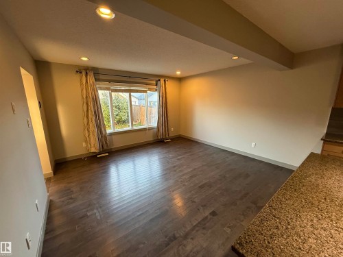Spacious room featuring dark wood-finish flooring, recessed lighting, and a large window - 7065 Cardinal Way Sw, Edmonton, AB 