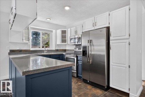 Kitchen featuring white and navy cabinetry, stainless steel appliances, dark stone flooring, and speckled countertops - 8 Wahstao Crescent Nw, Edmonton, AB 
