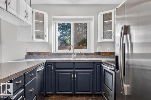 Kitchen featuring a dual basin sink, stainless steel appliances, dark wood-finish flooring, white upper cabinetry with reeded glass inserts, and dark lower cabinetry - 8 Wahstao Crescent Nw, Edmonton, AB 