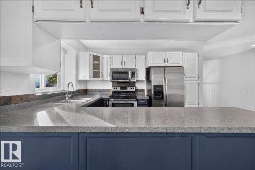 Kitchen featuring a blue-painted island, light-toned countertops, white cabinetry with hardware, a stainless steel refrigerator, and a stainless steel oven/range - 8 Wahstao Crescent Nw, Edmonton, AB 