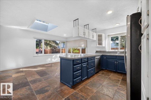 Kitchen featuring a central island, blue base cabinetry, light upper cabinetry, stainless steel appliances, and a skylight - 8 Wahstao Crescent Nw, Edmonton, AB 