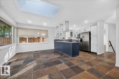 Kitchen featuring a skylight, slate tile flooring, white cabinetry, stainless steel appliances, and a central island with a dark countertop - 8 Wahstao Crescent Nw, Edmonton, AB 