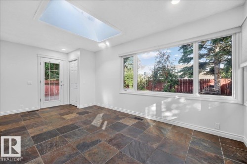 Spacious room featuring a skylight, expansive windows, a glass-paneled exterior door, and large-format tile flooring - 8 Wahstao Crescent Nw, Edmonton, AB 