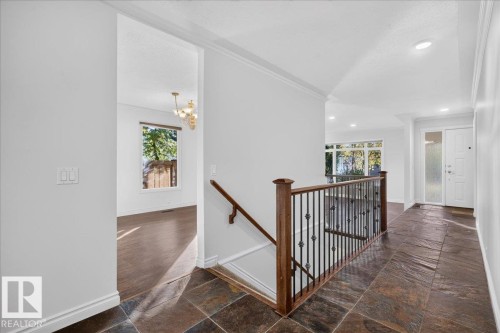 Dark slate tile flooring extending to the entry, wood-finish and wrought iron staircase railing, recessed lighting, white trim, and crown molding - 8 Wahstao Crescent Nw, Edmonton, AB 