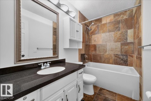 Bathroom featuring a white vanity with a dark countertop, an undermount sink, a framed mirror, a built-in shower/tub combination with full-height tile surround, and tile flooring - 8 Wahstao Crescent Nw, Edmonton, AB 