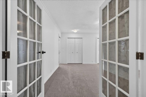 Dual French doors opening into a carpeted interior with neutral wall finishes, crown molding, and bi-fold closet doors - 8 Wahstao Crescent Nw, Edmonton, AB 