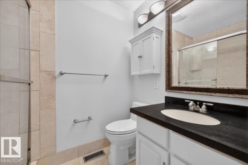 Shower with glass enclosure, light-toned tile surround, white vanity with dark countertop, undermount sink, and wall-mounted storage cabinet - 8 Wahstao Crescent Nw, Edmonton, AB 