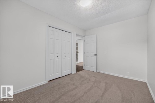 Neutral tone painted walls, light brown carpet flooring, white paneled bifold closet doors, white paneled interior door, and a flush mount ceiling light - 8 Wahstao Crescent Nw, Edmonton, AB 