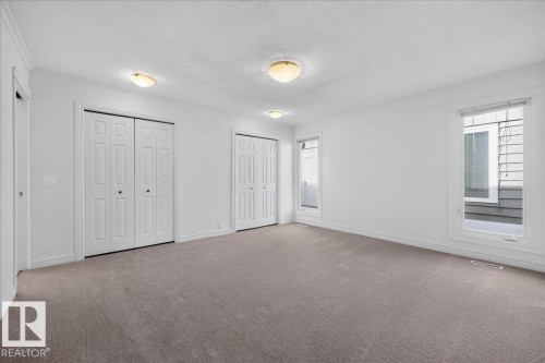 Spacious room featuring neutral carpeting, white walls, multiple windows, and two sets of bifold closet doors - 8 Wahstao Crescent Nw, Edmonton, AB 