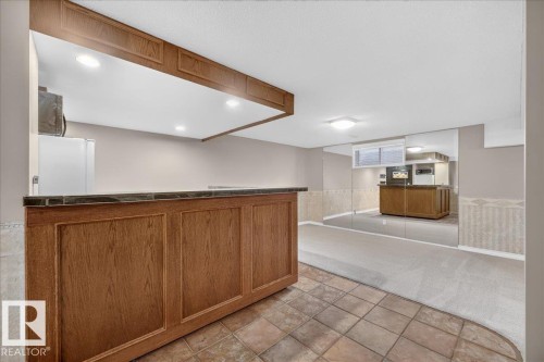Built-in wet bar with wood-finish cabinetry, tile countertop, and recessed lighting - 8 Wahstao Crescent Nw, Edmonton, AB 