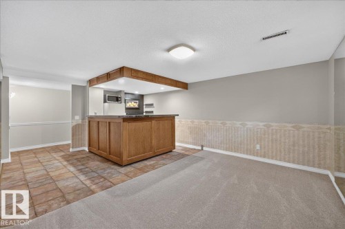 Built-in wet bar with wood cabinetry and countertop, recessed lighting, and integrated microwave - 8 Wahstao Crescent Nw, Edmonton, AB 