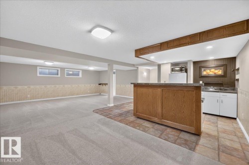 Spacious room with plush carpeting, recessed lighting, and a built-in bar featuring wood-finish cabinetry, a sink, and tile flooring - 8 Wahstao Crescent Nw, Edmonton, AB 