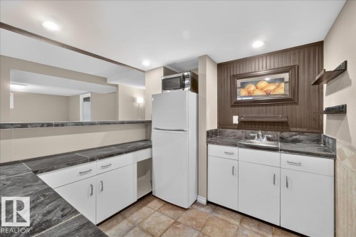 Built-in wet bar featuring a stainless steel sink, dark countertops, white cabinetry with silver hardware, and tile flooring - 8 Wahstao Crescent Nw, Edmonton, AB 