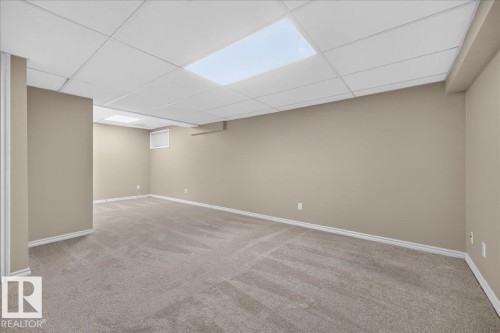 Spacious room with neutral-toned walls, gray-patterned carpet, white baseboards, and a dropped ceiling with integrated lighting - 8 Wahstao Crescent Nw, Edmonton, AB 