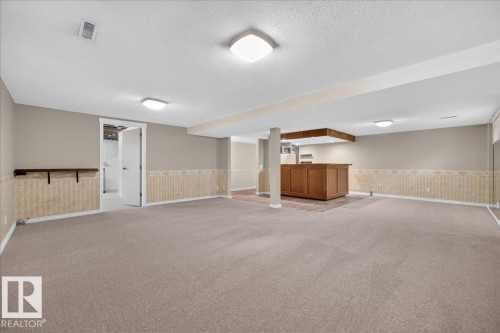 Spacious lower level featuring a built-in wood-finish bar and overhead cabinetry, light-toned carpeting, and a neutral wall palette - 8 Wahstao Crescent Nw, Edmonton, AB 
