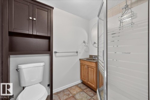 Ensuite bath in downstairs bedroom. Brown wood-finish built-in shelving, white toilet, wood-finish vanity with countertop, glass shower enclosure, and textured flooring - 8 Wahstao Crescent Nw, Edmonton, AB 