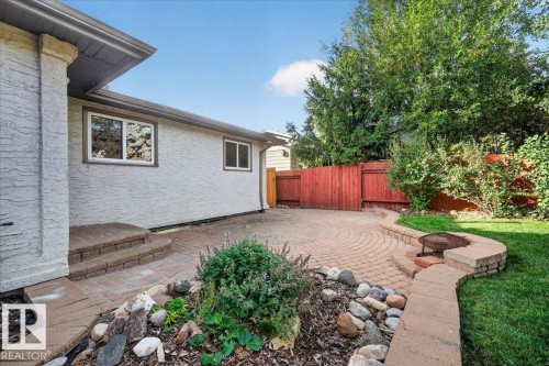 Stucco exterior with brown trim windows, brick paver patio, stone retaining wall, and a built-in fire pit - 8 Wahstao Crescent Nw, Edmonton, AB 