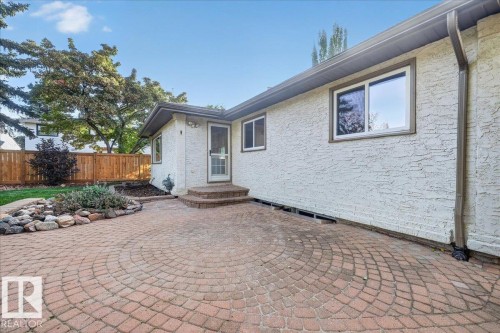Textured stucco exterior with multiple windows, a wood fence, and a brick paver patio featuring a radial pattern - 8 Wahstao Crescent Nw, Edmonton, AB 