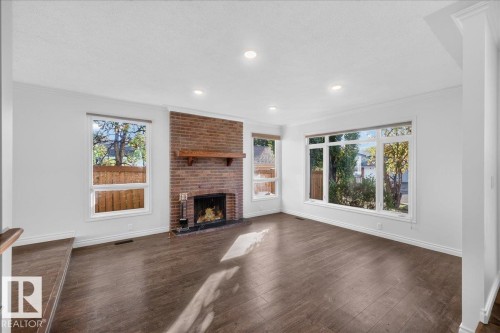 Spacious room featuring wood-finish flooring, a brick fireplace with a wood mantle, and multiple large windows - 8 Wahstao Crescent Nw, Edmonton, AB 