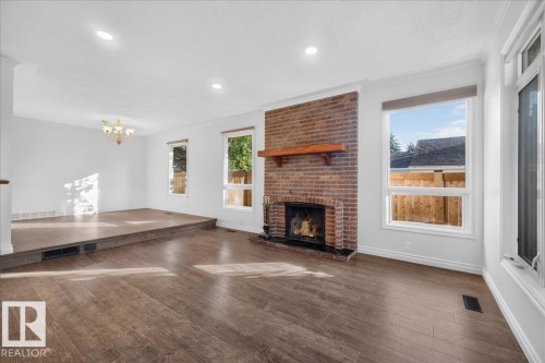 Brick fireplace with a wood mantle, wood-finish flooring, recessed lighting, and multiple windows - 8 Wahstao Crescent Nw, Edmonton, AB 