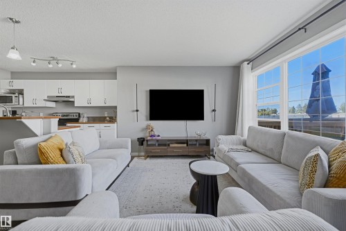 Open-concept living space featuring a kitchen with white cabinetry and wood-finish countertops, large windows, and a ceiling-mounted track light fixture - 3151 Trelle Loop Nw, Edmonton, AB 