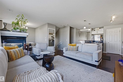Open-concept living area featuring a fireplace with white mantel, dark wood-finish flooring, recessed lighting, and a kitchen island with seating - 3151 Trelle Loop Nw, Edmonton, AB 