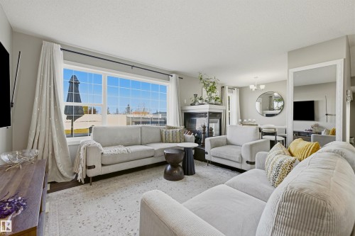 Spacious living area featuring large picture windows, wood-finish flooring, a corner fireplace with a white mantel, and recessed lighting - 3151 Trelle Loop Nw, Edmonton, AB 