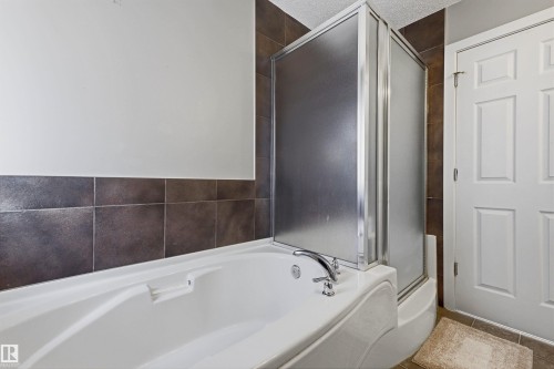 White soaking tub with chrome fixtures, enclosed shower, and dark tile surround - 3151 Trelle Loop Nw, Edmonton, AB 