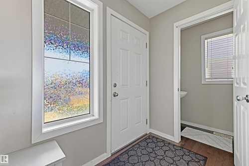 Entryway featuring wood-finish flooring, a white paneled door, and an adjacent room with a pedestal sink and window with blinds - 3151 Trelle Loop Nw, Edmonton, AB 