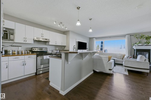 Open-concept living area featuring wood-finish flooring, white cabinetry, stainless steel appliances, and a fireplace with a mantel - 3151 Trelle Loop Nw, Edmonton, AB 