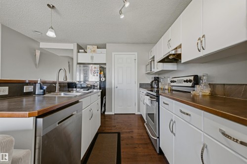 Kitchen featuring white cabinetry, dark wood-finish countertops, stainless steel appliances, and wood-finish flooring - 3151 Trelle Loop Nw, Edmonton, AB 
