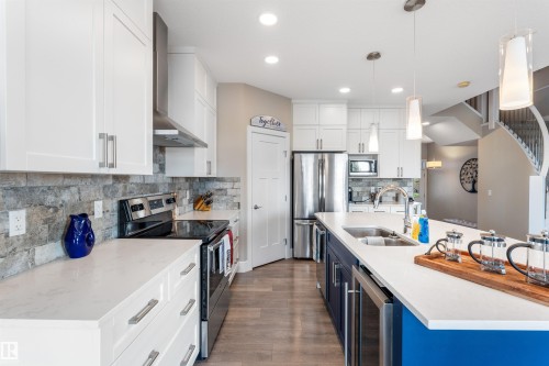 White shaker cabinetry, stone backsplash, stainless steel appliances, wood-finish flooring, and a kitchen island with built-in sink - 3334 Parker Loop Sw, Edmonton, AB 