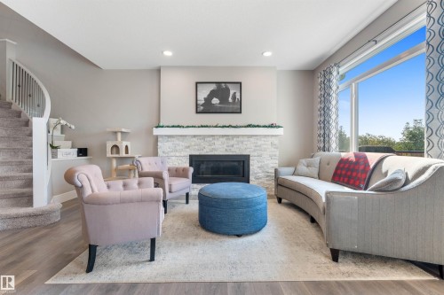 Open-concept living space featuring wood-finish flooring, a contemporary fireplace with a stone surround, and a large window - 3334 Parker Loop Sw, Edmonton, AB 