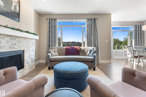 Stacked stone fireplace with a white mantel, wood-finish flooring, and expansive windows - 3334 Parker Loop Sw, Edmonton, AB 