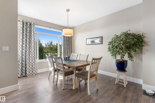 Expansive dining area featuring wood-finish flooring, a large window, and a drum pendant light fixture - 3334 Parker Loop Sw, Edmonton, AB 