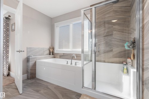 Built-in bathtub with deck-mounted faucet, glass-enclosed shower with tiled walls, and window with horizontal blinds - 3334 Parker Loop Sw, Edmonton, AB 