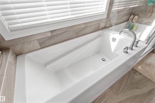 White soaking tub featuring a chrome faucet, light-toned wood-finish tile surround, and a clear glass shower enclosure - 3334 Parker Loop Sw, Edmonton, AB 