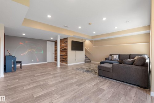 Expansive open-concept room with LED lighting, wood-finish flooring, and a textured wood accent wall - 3334 Parker Loop Sw, Edmonton, AB 