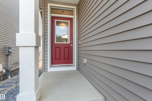 Red entry door with an overhead transom window, concrete porch, and white structural column - 3334 Parker Loop Sw, Edmonton, AB 