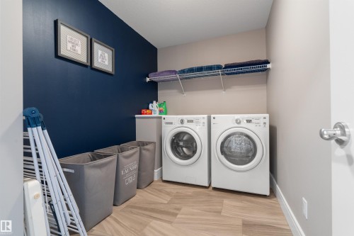 Laundry area with wood-look tile flooring, blue accent wall, and a built-in wire shelf - 3334 Parker Loop Sw, Edmonton, AB 